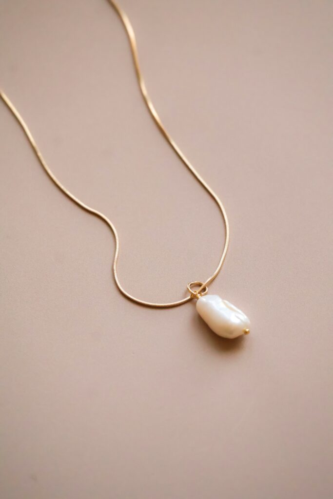 Gold chain necklace with a large baroque pearl pendant on a light beige background