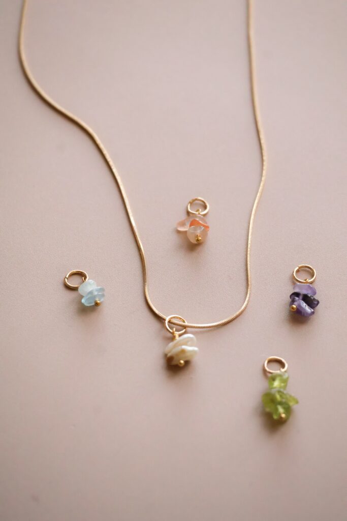 Gold chain necklace with small pastel gemstone pendants laid on a pale background, multiple colors visible (blue, pink, purple, green).