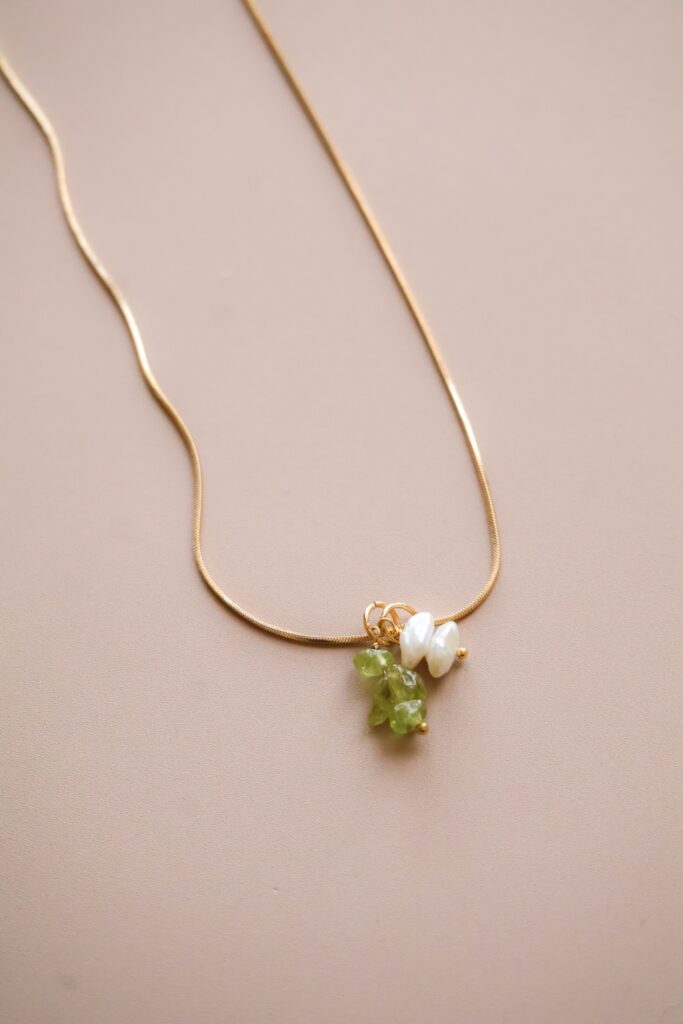 Gold chain necklace with a pendant of white pearls and green stones on a beige background