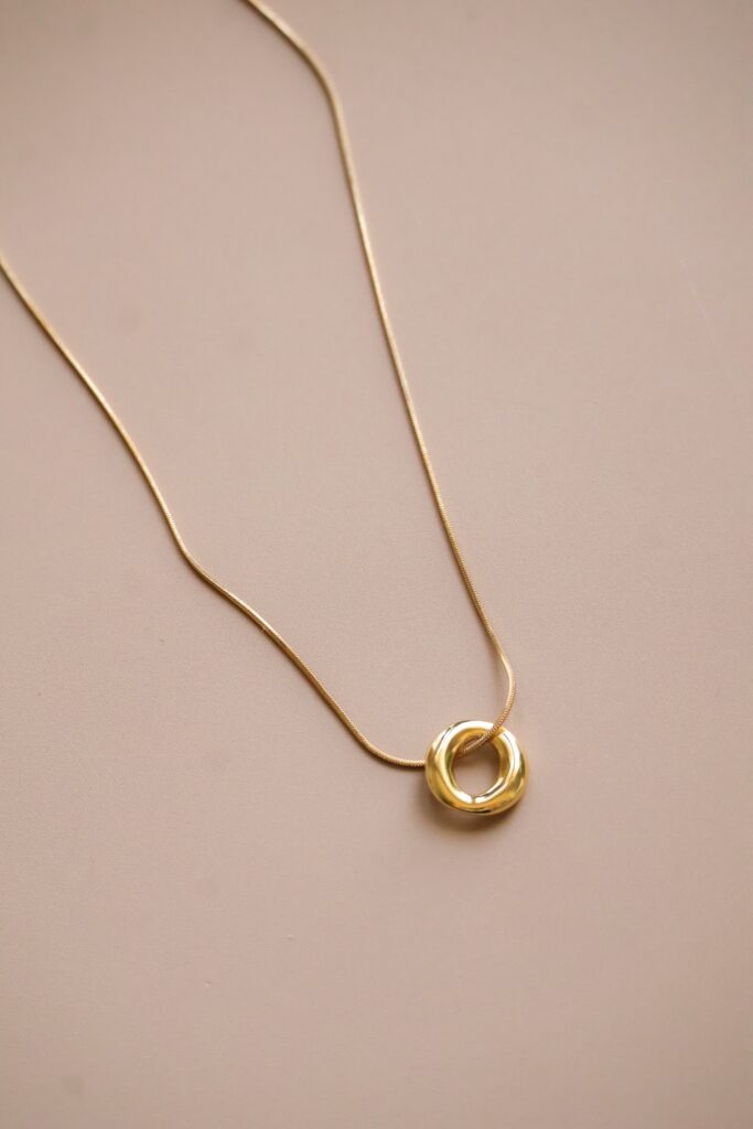 Gold chain with a hollow circular pendant resting on a beige background.